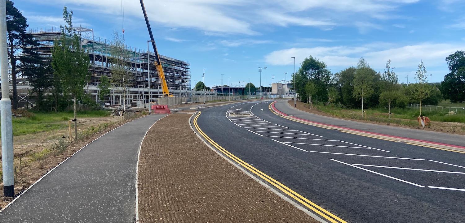 View
                          along new road with stretch of bare soil
                          between it and a footway on the left