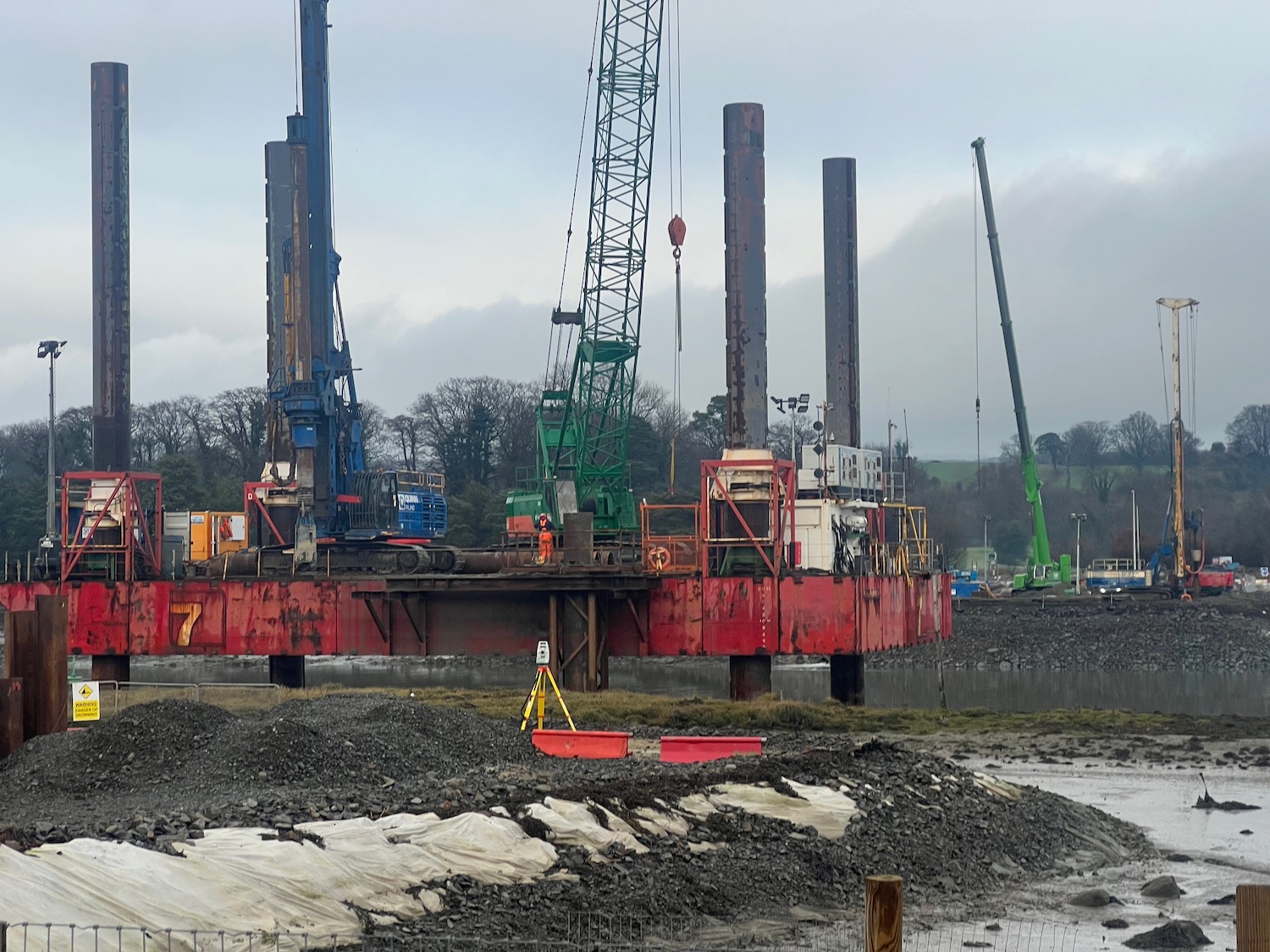 Ground level view of a red platform with
                          four long legs extending into the air, with a
                          crane and a pile driver on the platform.