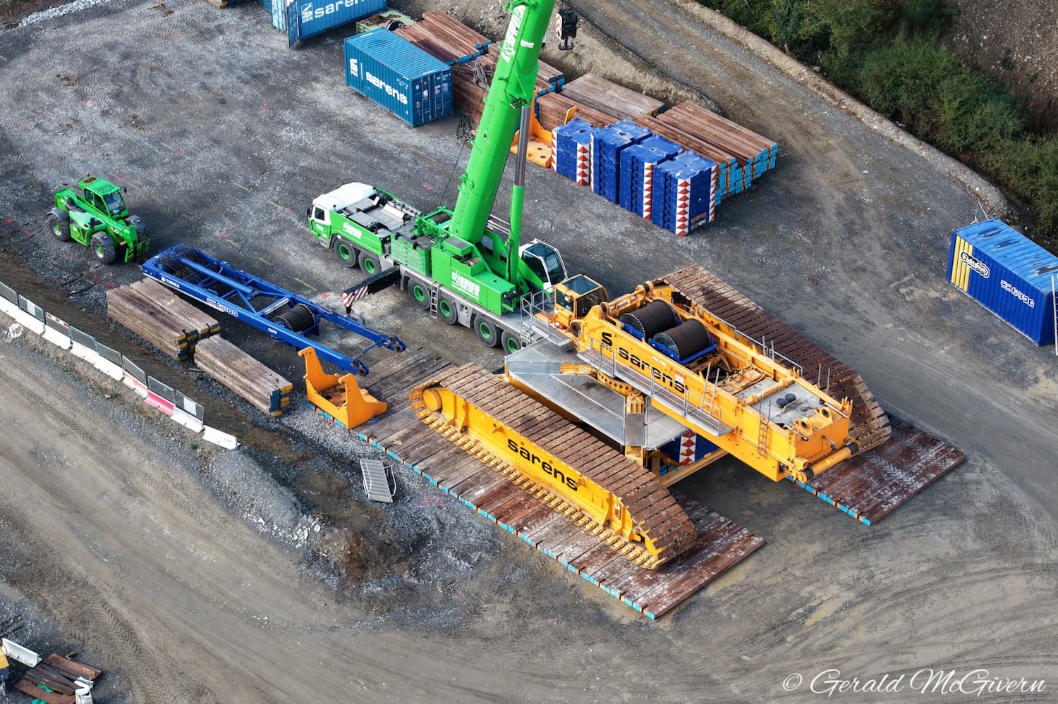 Two large yellow caterpillar tracks side
                          by side on a temporary playform, with a
                          smaller crane lifting components on top of
                          it.