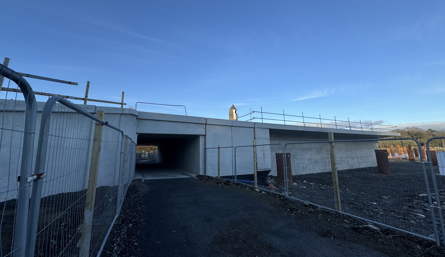 View from ground level with the grey,
                          concrete abutment running left-right. Straight
                          ahead a path goes into a rectangular tunnel
                          under the abutment.